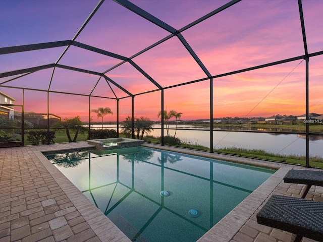 pool at dusk with a patio area, an in ground hot tub, a water view, and glass enclosure