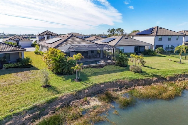 rear view of house with a water view, a lanai, a lawn, and solar panels