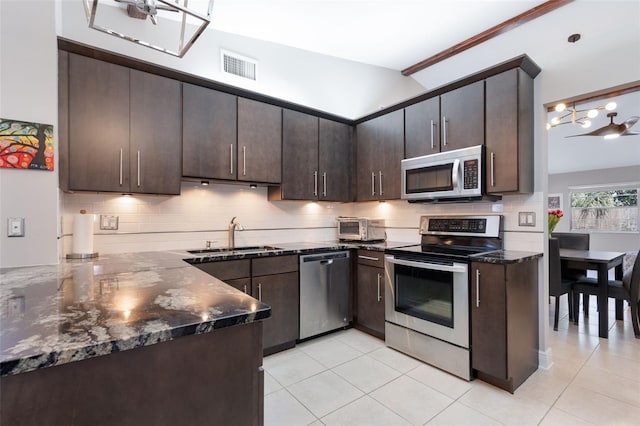 kitchen with dark brown cabinetry, sink, light tile patterned floors, appliances with stainless steel finishes, and dark stone counters