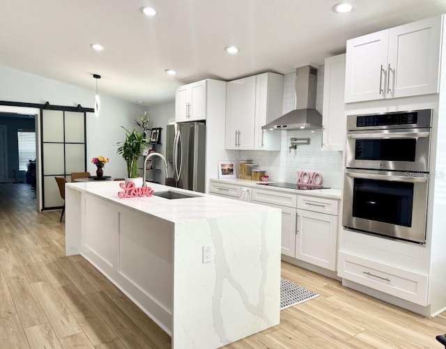 kitchen featuring tasteful backsplash, white cabinetry, stainless steel appliances, a barn door, and wall chimney exhaust hood