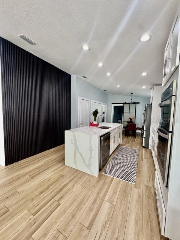 kitchen featuring white cabinetry, appliances with stainless steel finishes, light stone countertops, and a center island with sink