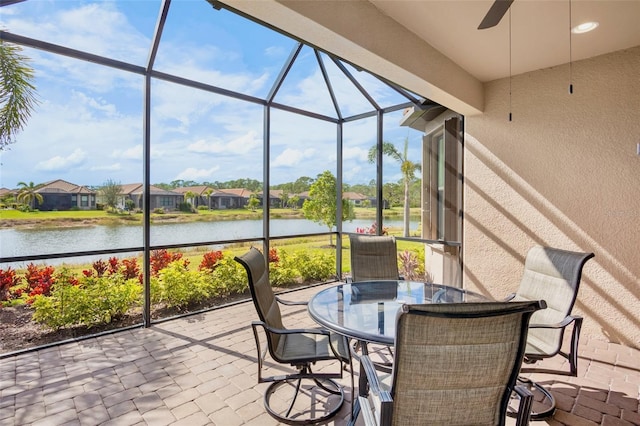 view of patio with ceiling fan, glass enclosure, and a water view