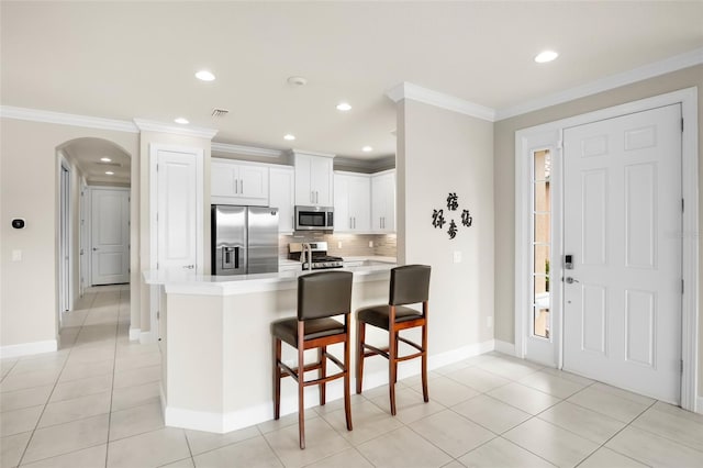 kitchen with white cabinetry, a kitchen bar, kitchen peninsula, stainless steel appliances, and crown molding