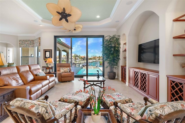 living room featuring light tile patterned flooring, ceiling fan, ornamental molding, and a tray ceiling