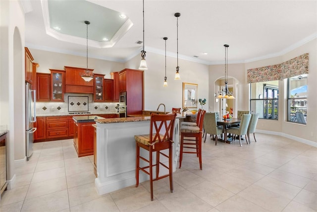 kitchen with crown molding, stone countertops, decorative light fixtures, a tray ceiling, and stainless steel appliances