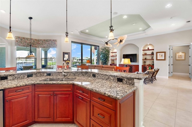 kitchen with built in shelves, sink, light stone counters, hanging light fixtures, and a tray ceiling