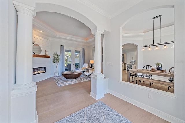 foyer entrance with crown molding, light hardwood / wood-style flooring, decorative columns, a tray ceiling, and a fireplace