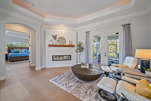 sitting room with ornamental molding, a large fireplace, light hardwood / wood-style floors, a raised ceiling, and french doors