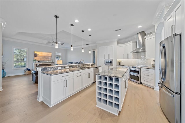 kitchen featuring decorative light fixtures, appliances with stainless steel finishes, a kitchen island, wall chimney range hood, and white cabinets