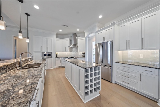 kitchen with sink, white cabinetry, hanging light fixtures, appliances with stainless steel finishes, and wall chimney range hood