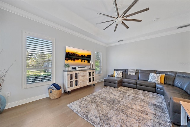 living room featuring a raised ceiling, wood-type flooring, ornamental molding, and ceiling fan