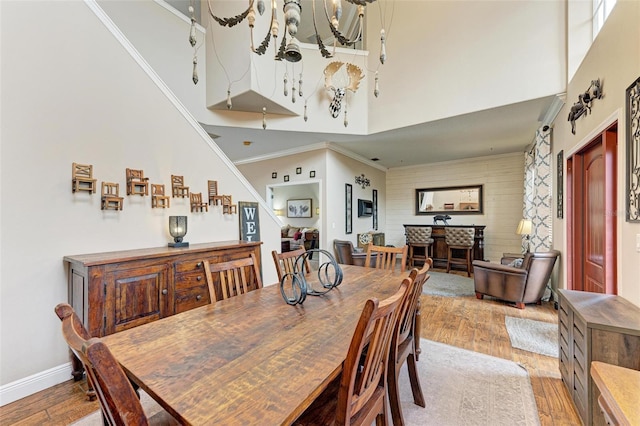 dining area with ornamental molding, a notable chandelier, a towering ceiling, a fireplace, and light hardwood / wood-style floors