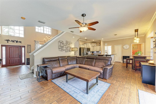 living room featuring ceiling fan with notable chandelier, ornamental molding, light hardwood / wood-style floors, and a textured ceiling