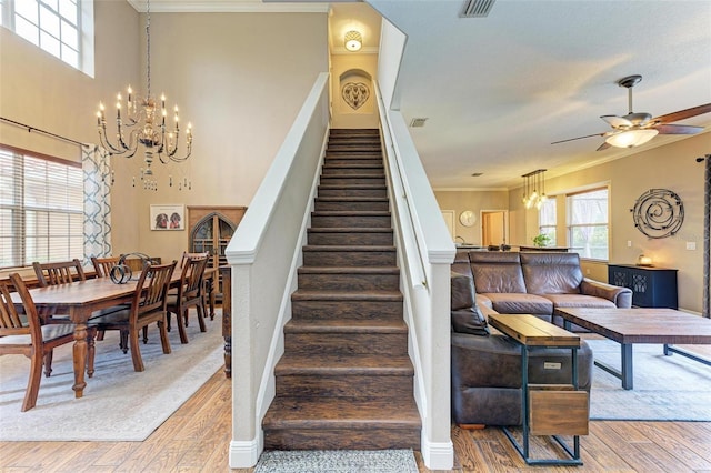 staircase featuring hardwood / wood-style flooring, ceiling fan with notable chandelier, and ornamental molding