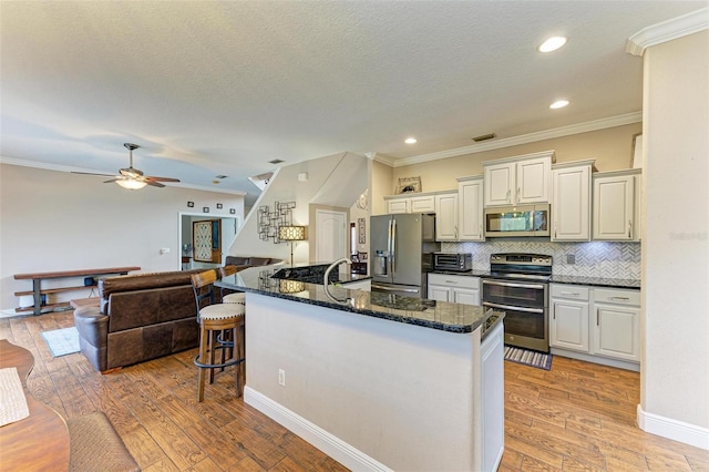 kitchen with backsplash, light hardwood / wood-style floors, dark stone counters, and appliances with stainless steel finishes