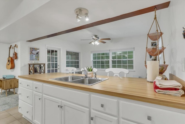 kitchen with wood counters, sink, white cabinets, hanging light fixtures, and light tile patterned floors