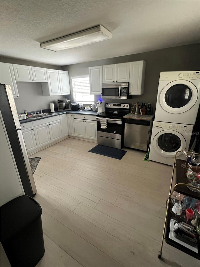 kitchen featuring stacked washing maching and dryer, appliances with stainless steel finishes, sink, white cabinets, and light hardwood / wood-style flooring