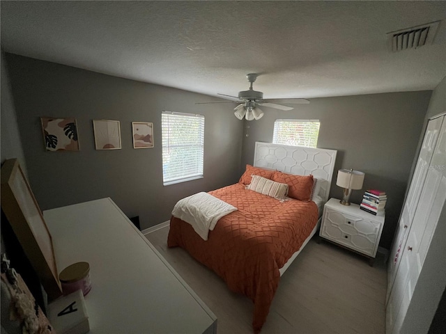 bedroom featuring multiple windows, a textured ceiling, ceiling fan, and light hardwood / wood-style flooring