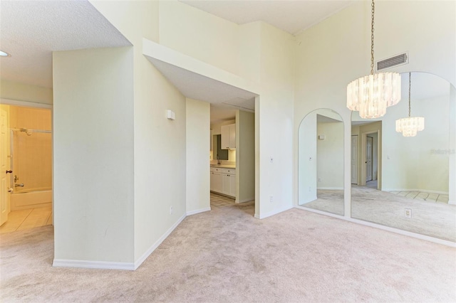 spare room featuring a high ceiling, light colored carpet, and a chandelier