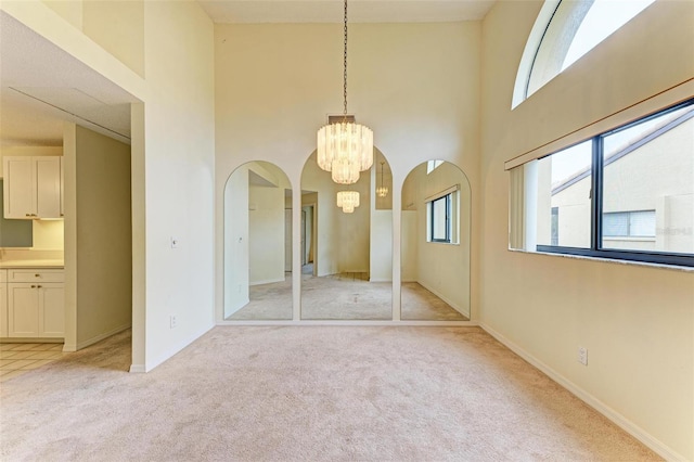 interior space featuring multiple windows, a notable chandelier, light colored carpet, and a high ceiling