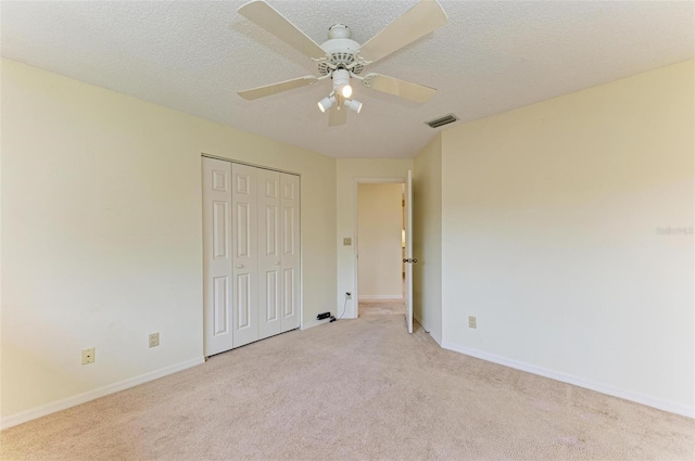 unfurnished bedroom with ceiling fan, light carpet, a textured ceiling, and a closet