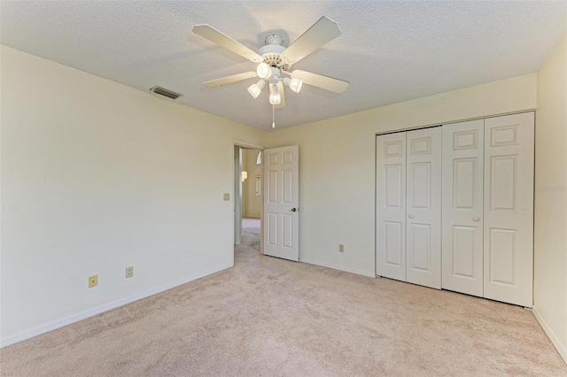 unfurnished bedroom with ceiling fan, light colored carpet, a closet, and a textured ceiling