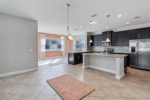 kitchen with appliances with stainless steel finishes, an island with sink, sink, backsplash, and hanging light fixtures