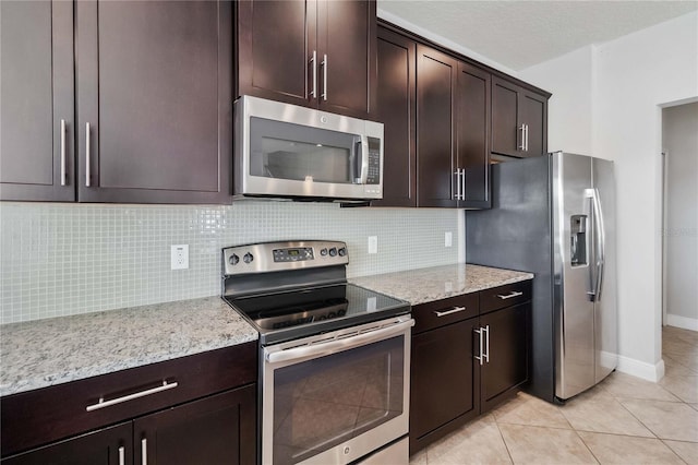 kitchen with light tile patterned floors, appliances with stainless steel finishes, backsplash, dark brown cabinetry, and light stone counters