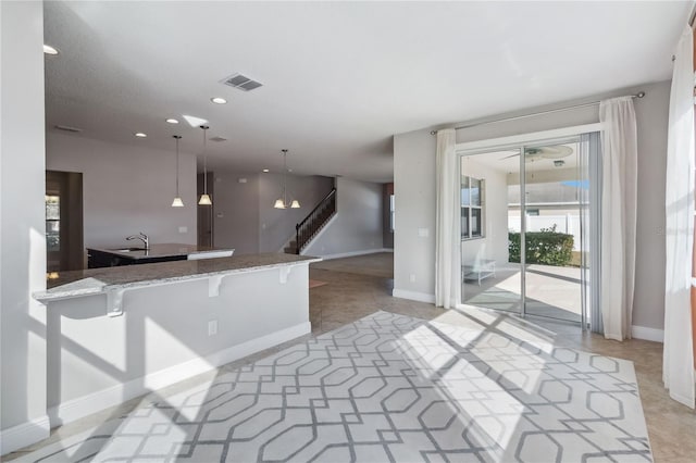 kitchen featuring sink, a kitchen breakfast bar, light stone counters, decorative light fixtures, and kitchen peninsula