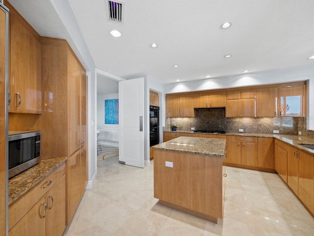 kitchen with gas stovetop, tasteful backsplash, a center island, double oven, and light stone countertops