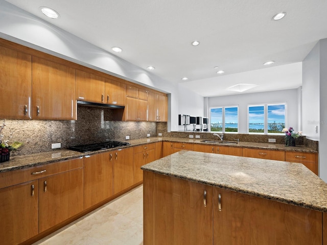 kitchen with sink, tasteful backsplash, a kitchen island, stone counters, and black gas stovetop