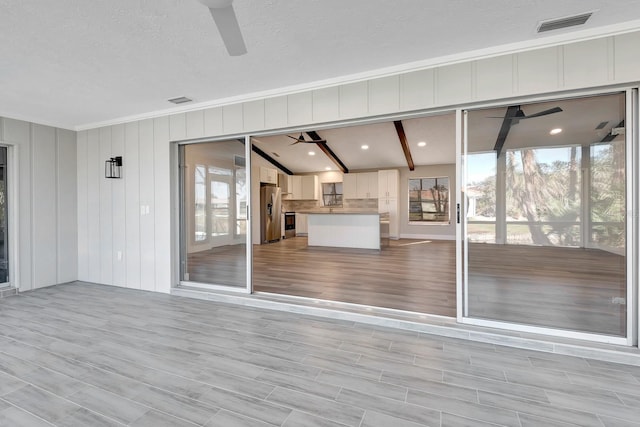 interior space with beamed ceiling, ceiling fan, and light wood-type flooring