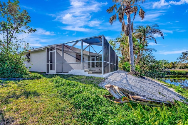 rear view of property featuring a lawn, glass enclosure, and a water view