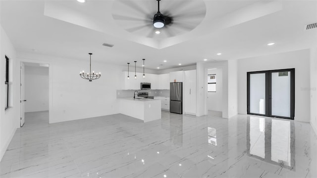 kitchen featuring stainless steel appliances, white cabinetry, open floor plan, a raised ceiling, and decorative light fixtures