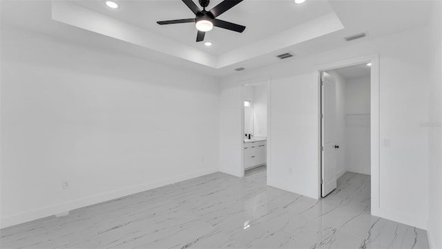 unfurnished bedroom featuring a tray ceiling, a walk in closet, visible vents, and baseboards