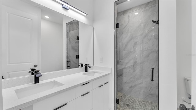 bathroom with double vanity, a marble finish shower, a sink, and toilet