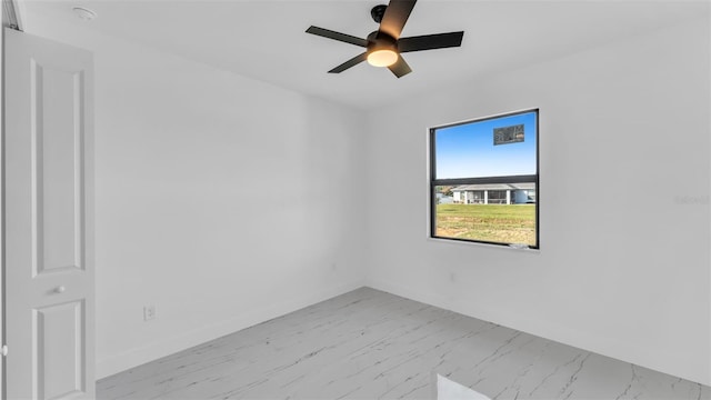 unfurnished room with marble finish floor, a ceiling fan, and baseboards