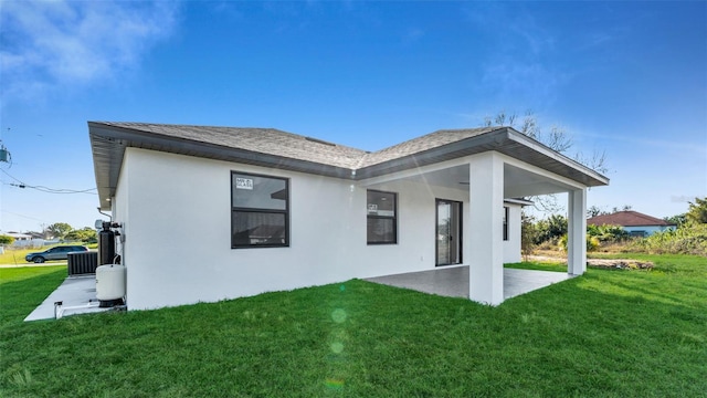 back of property featuring a yard, stucco siding, a shingled roof, central AC unit, and a patio area