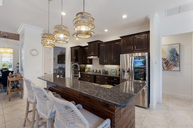 kitchen with dark stone countertops, decorative light fixtures, an island with sink, and appliances with stainless steel finishes