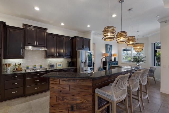 kitchen featuring appliances with stainless steel finishes, a breakfast bar area, dark stone counters, hanging light fixtures, and a center island with sink