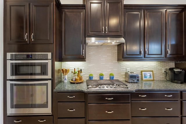 kitchen featuring dark stone countertops, backsplash, dark brown cabinets, and appliances with stainless steel finishes