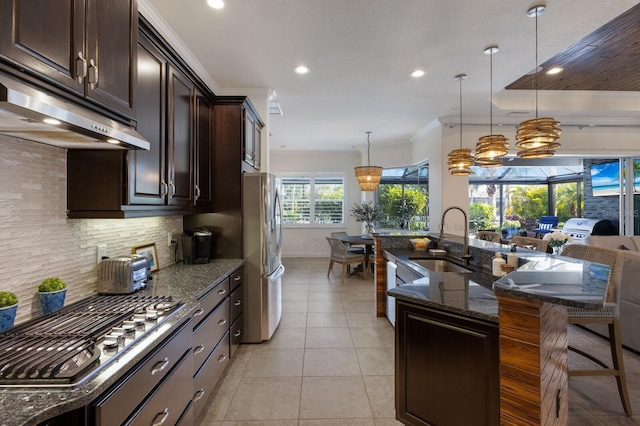 kitchen featuring sink, appliances with stainless steel finishes, dark stone countertops, a kitchen bar, and decorative light fixtures