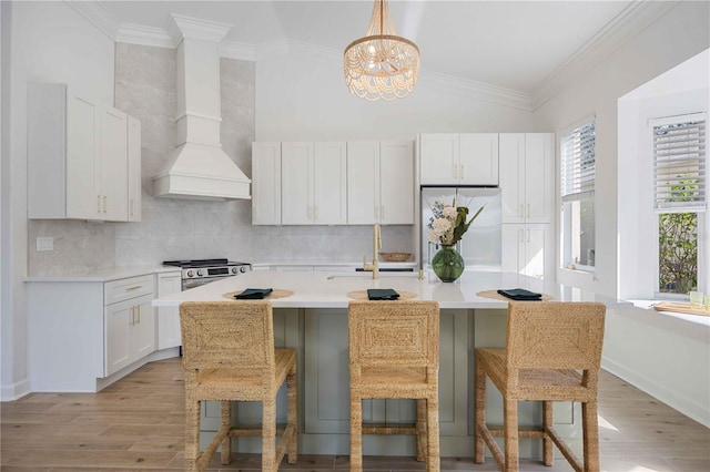 kitchen with refrigerator, decorative light fixtures, a breakfast bar area, white cabinets, and custom exhaust hood