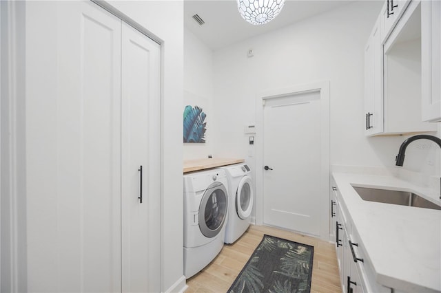 laundry area with visible vents, light wood-style flooring, separate washer and dryer, cabinet space, and a sink