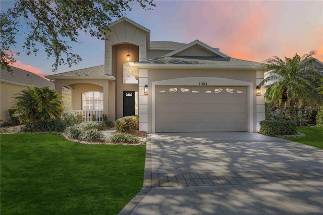 view of front of home featuring a shingled roof, a front yard, stucco siding, decorative driveway, and a garage