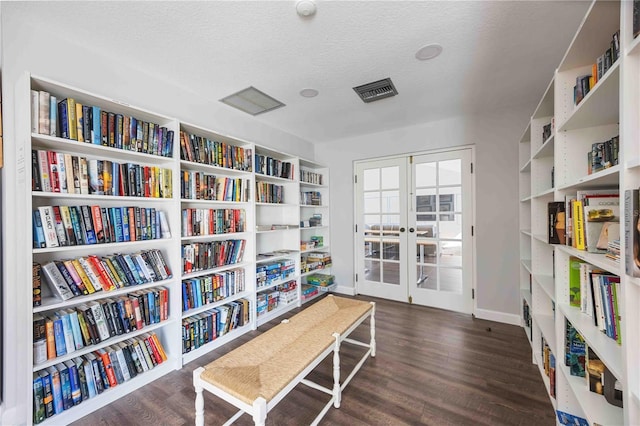 living area with visible vents, wall of books, french doors, wood finished floors, and a textured ceiling