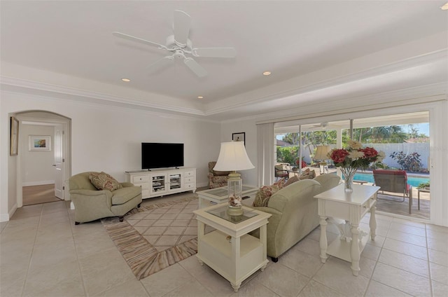 living room with light tile patterned floors, a tray ceiling, ornamental molding, and ceiling fan