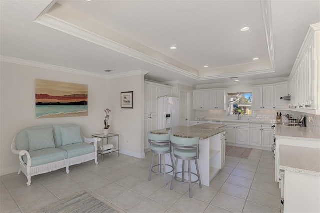 kitchen featuring a center island, ornamental molding, a raised ceiling, white fridge with ice dispenser, and white cabinets