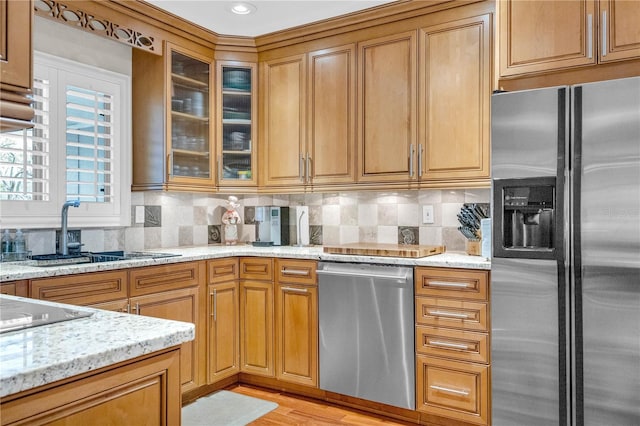 kitchen with light stone counters, appliances with stainless steel finishes, tasteful backsplash, and light wood-type flooring