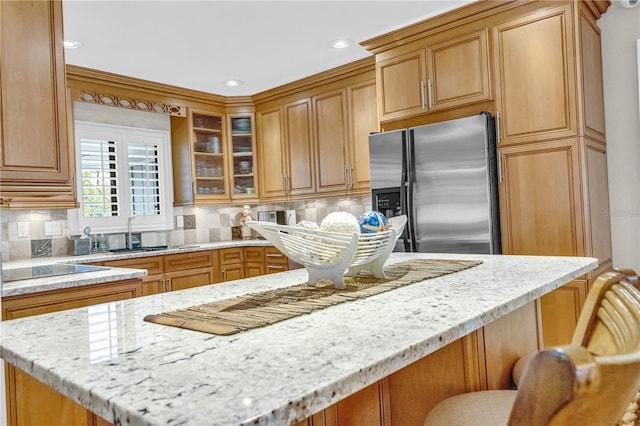 kitchen featuring a sink, black electric stovetop, stainless steel fridge, and light stone counters